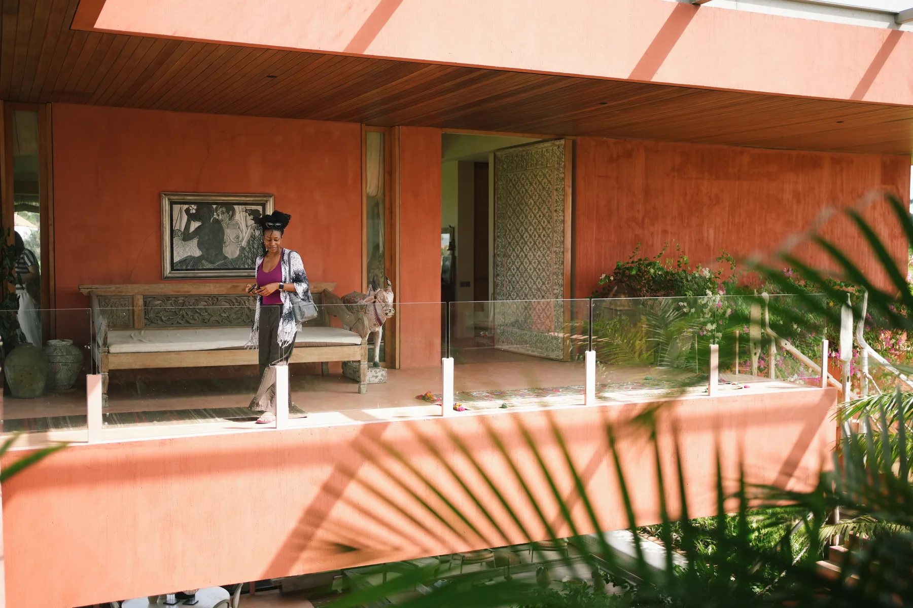 A student standing on an open terracotta-toned corridor at Nenek Coco Villa, a carved wooden bench behind her