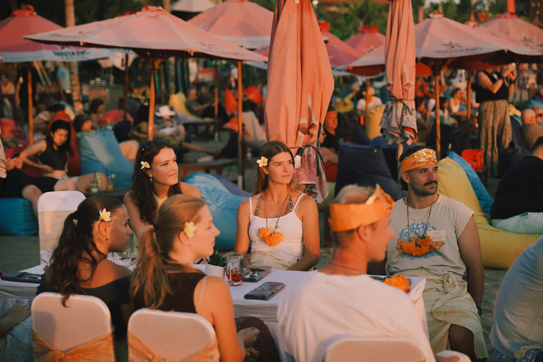 A group of students seated at a dinner table on the beach, talking before the meal